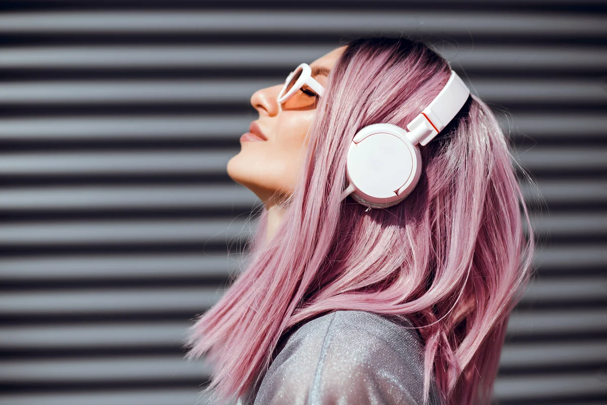 Young woman with purple pink hair listening to music on headphones