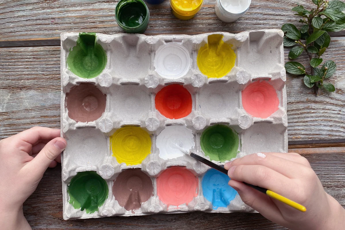 Children's hands paint colored eggs box