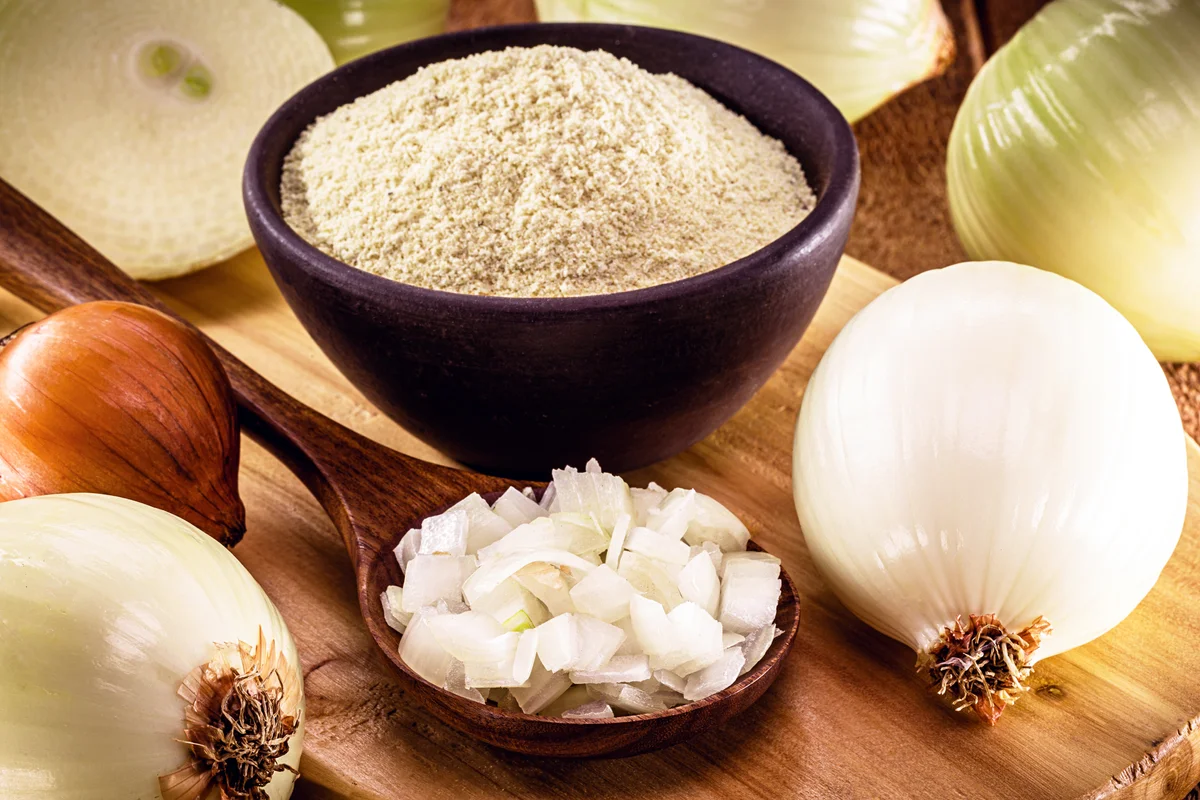 Wooden spoon with sliced ​​onion and bowl with powdered onion