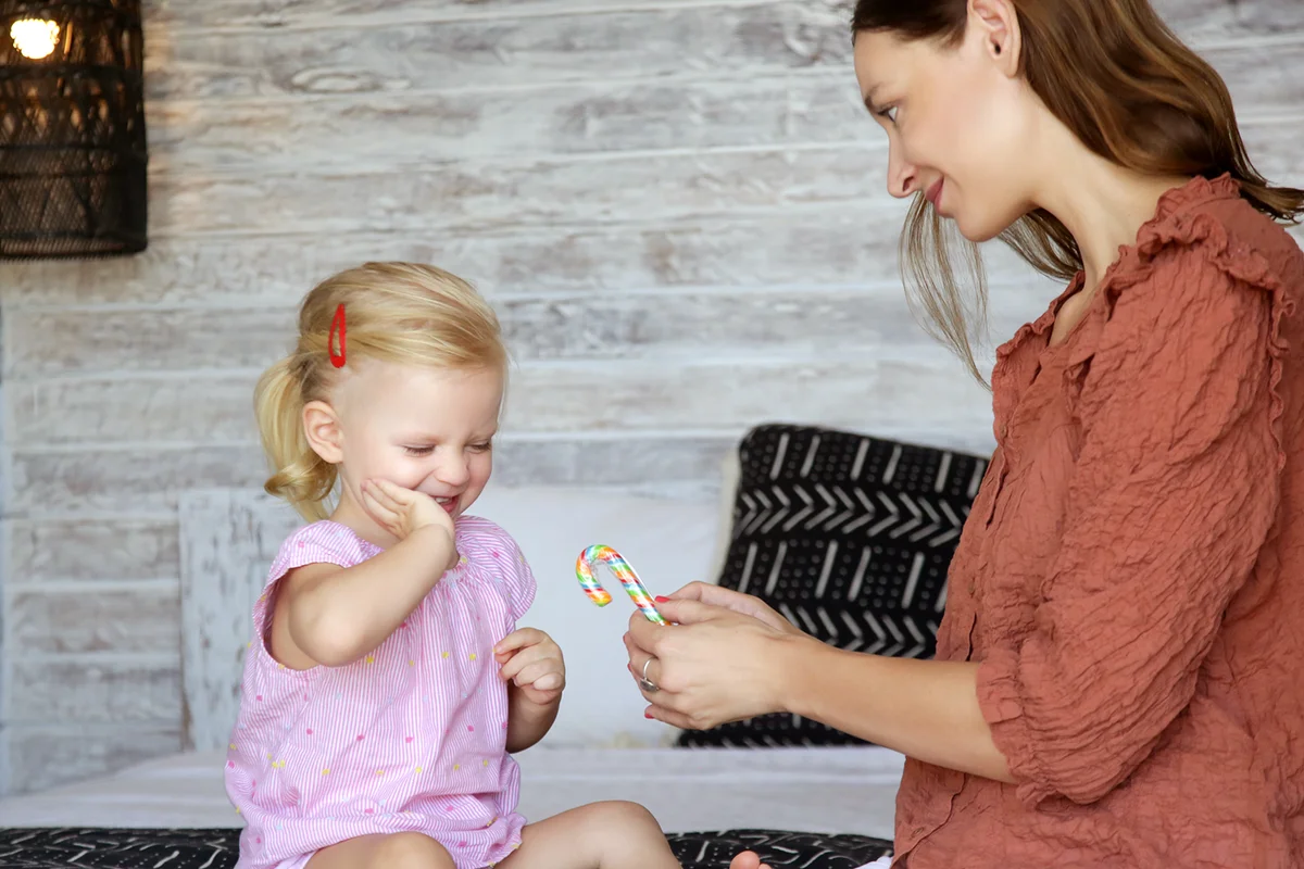 Mother giving rainbow lollipop candy to her toddler