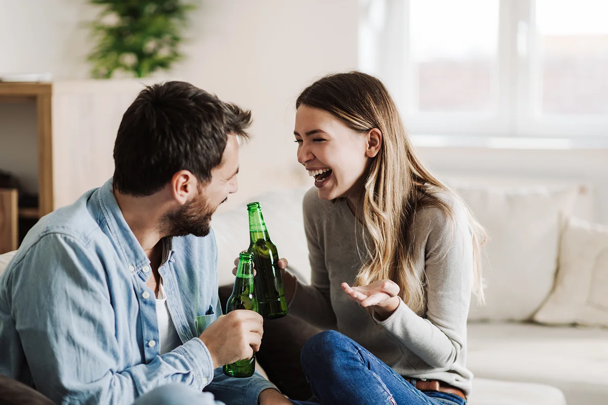 Young happy couple sitting on the sofa and drinking beer