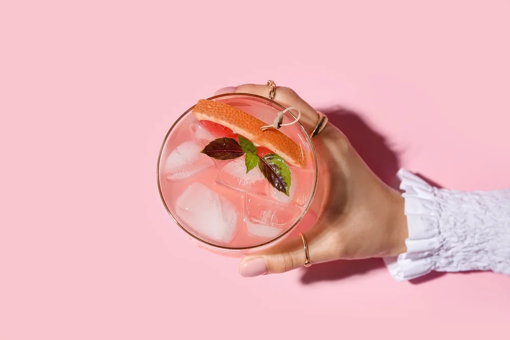 Women's hand holding a pink, fruity drink with a pink background