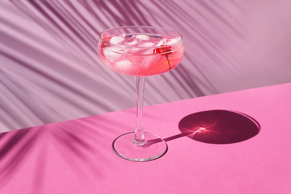A cup of pink gin in a pink background, with a flower petal inside