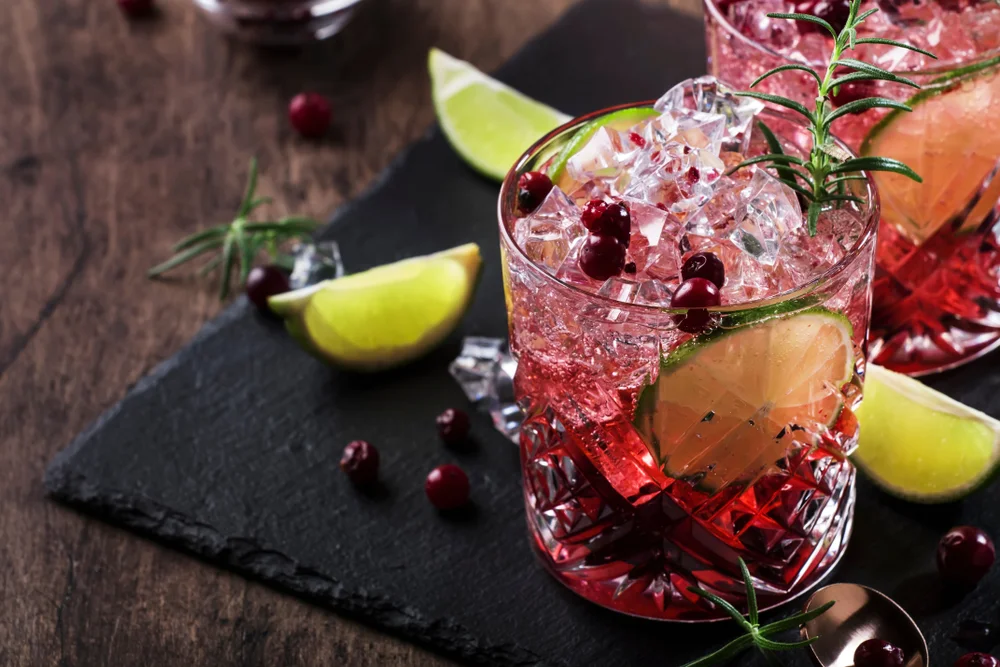 Pink spritz cocktail with crushed ice and bar tools on grey background