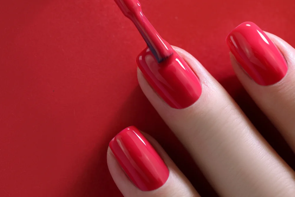 Close detail shot of nails being painted red on a red background