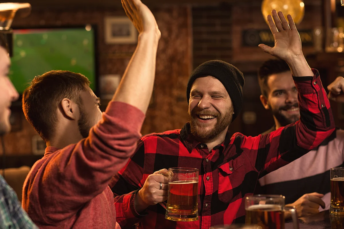 men laughing high fiving his friend while having beer at the pub together
