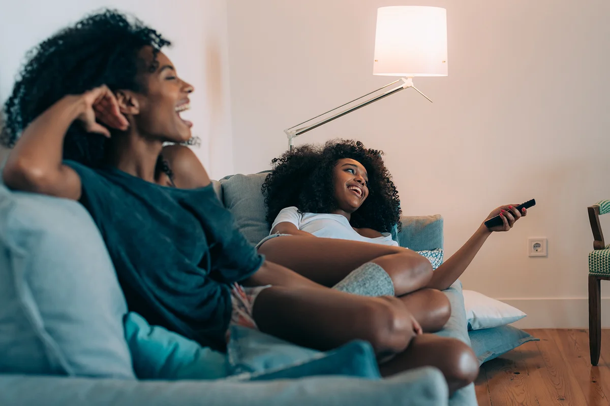 Happy young women lying down in the couch watching tv