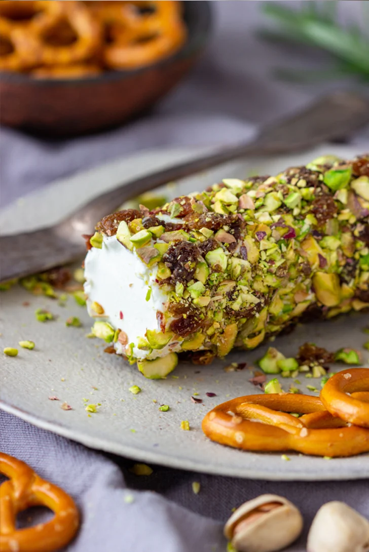 Detail of a cheese log on a plate with tools and other snacks