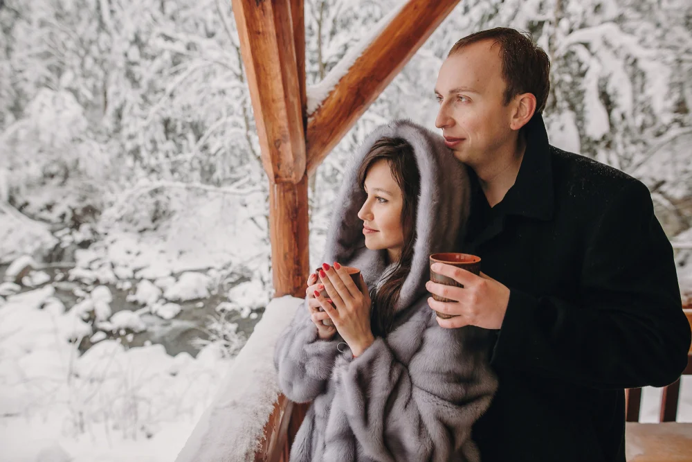 Couple hugging in a balcony in winter and holding warm drinks