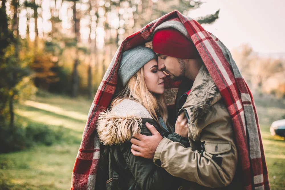 Couple hugging covered with plaid blanket in the forest