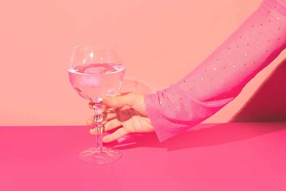 Pink gin cocktail in a highball glass and female hand