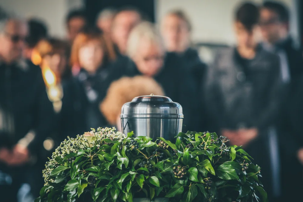 Urn over plant decorations and people out of focus in the background at a funeral