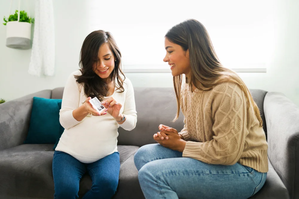 Happy pregnant woman talking to her friend at home