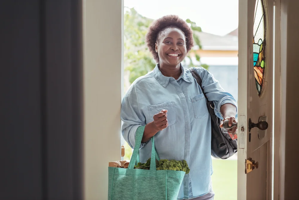 Smiley woman walking through the house door with groceries