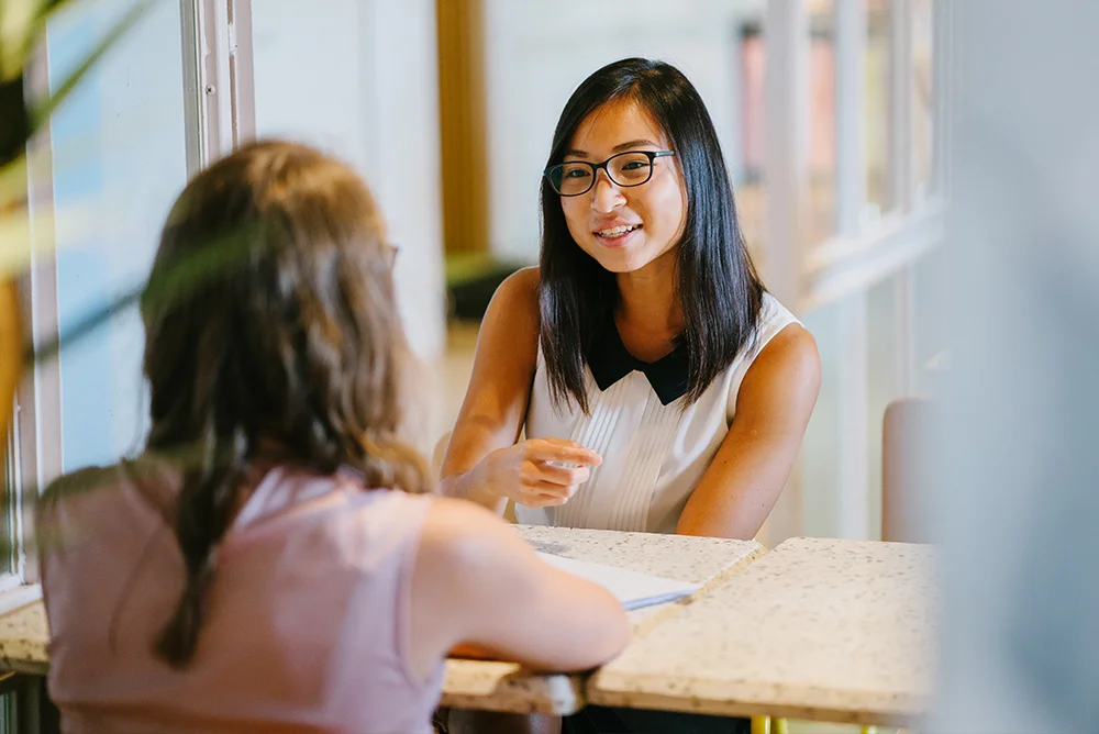 Two young women sitting across each other talking