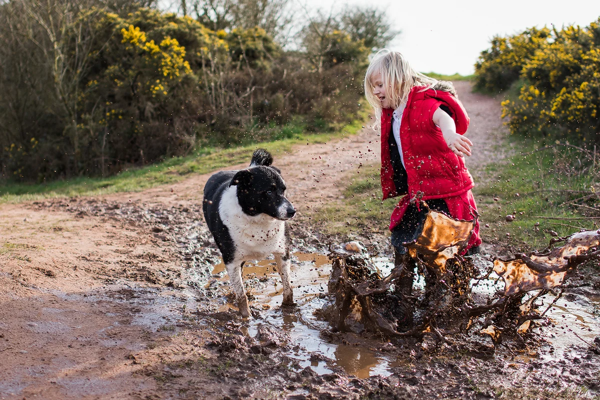 girl jumping in very muddy puddle with her dog
