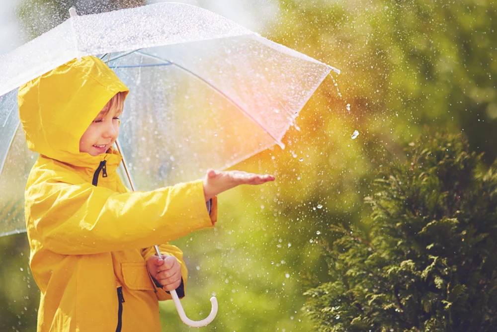 Happy kid with umbrella and rain coat catching spring rain drops their hand