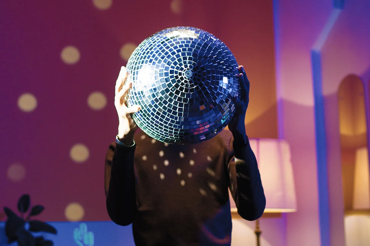 young male standing in room in evening at home holding big disco ball