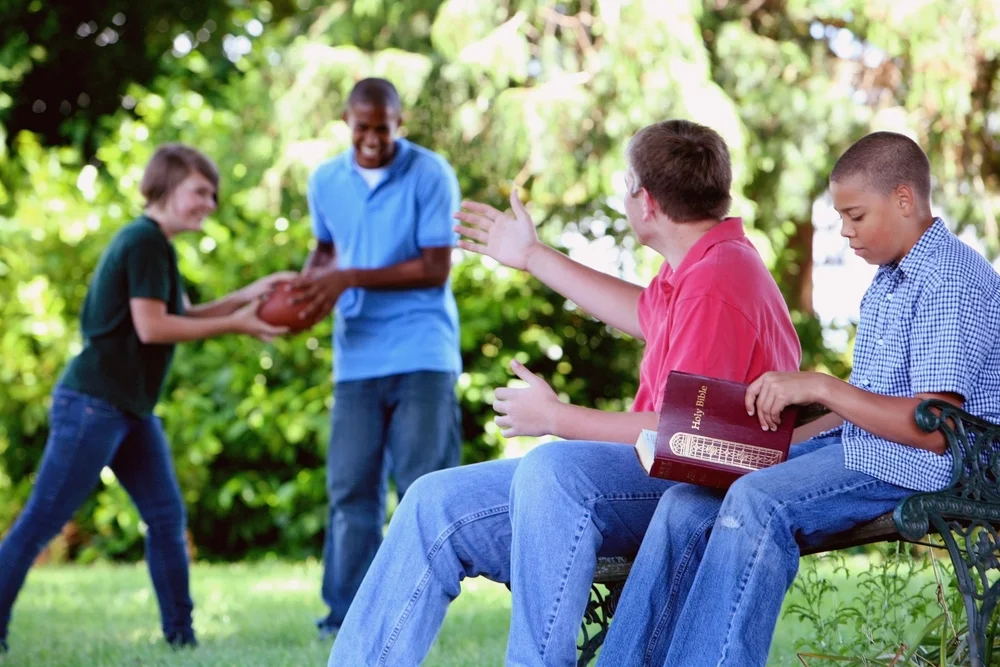 Teens playing football and reading the bible in a park