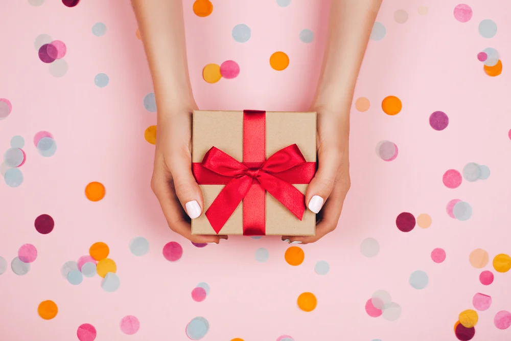 Woman's hands holding gift box surrounded by confetti