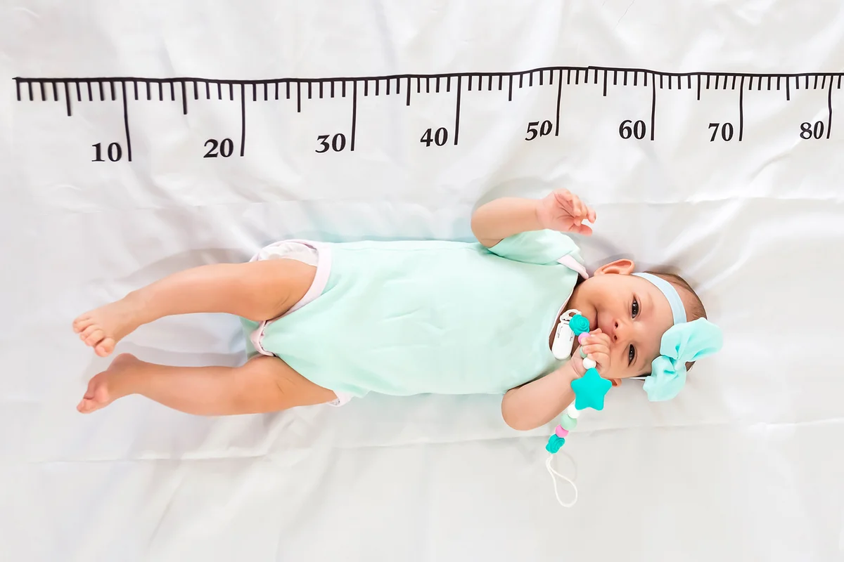 A three month baby in mint green clothes lying on a bed
