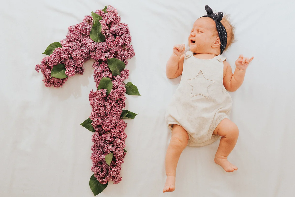 Flat lay picture of a 1 month baby with number made out of oak leaves and lilac flower