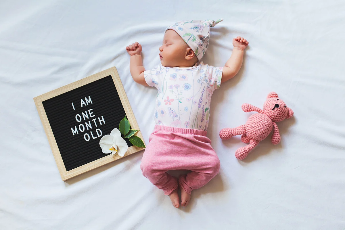 Portrait of sleeping one month old newborn baby girl laying between letter board and teddy bear