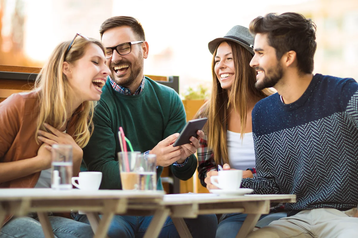 Two women and two men at cafe talking laughing and enjoying their time using digital tablet.