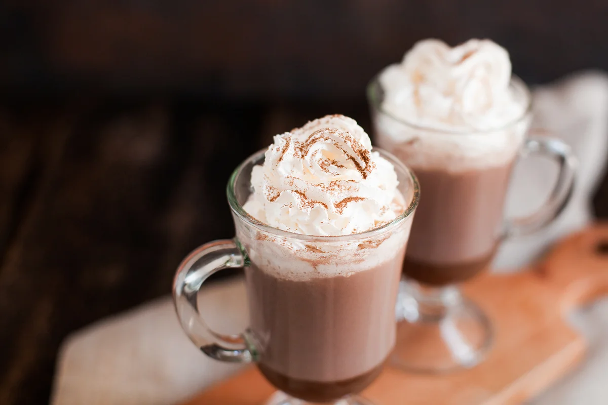 Two glasses with Hot chocolate garnished with whipped cream and cocoa powder