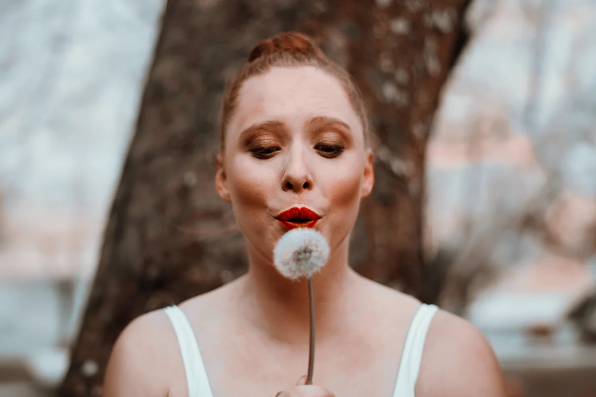 Female ballet dancer blowing a dandelion flower and it's seeds