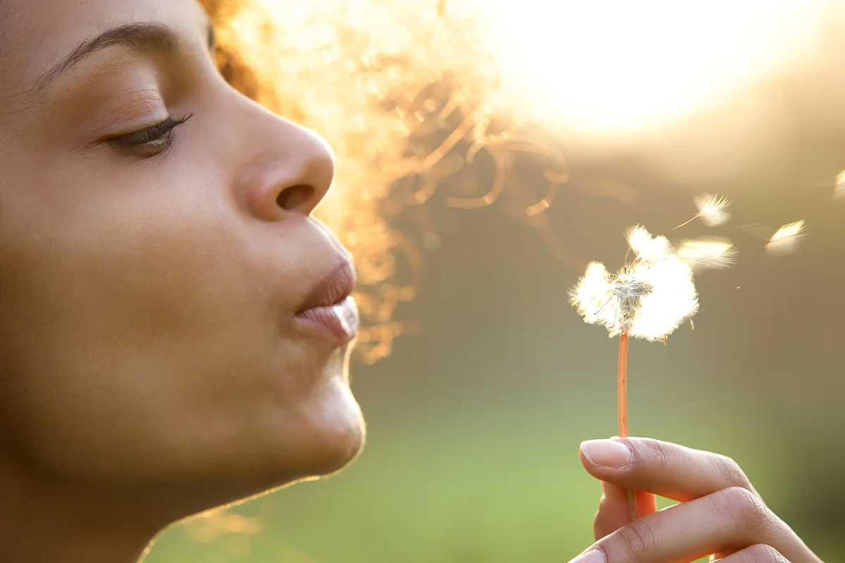 Portrait of a beautiful young woman blowing dandelion flower