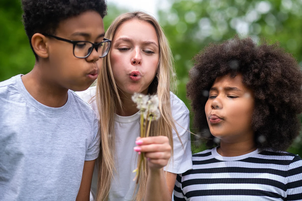 Blonde girls and two african american kids blowing on dandelion