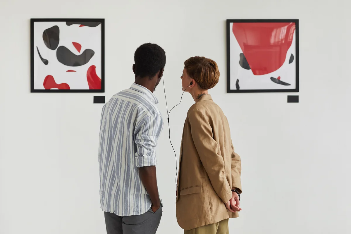 Graphic back view portrait of two young people looking at paintings and sharing audio guide