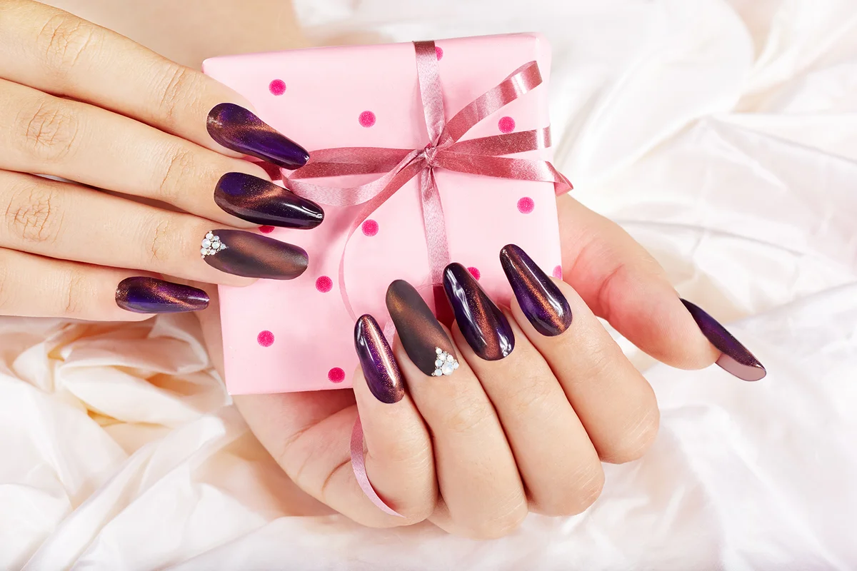Hands with long artificial manicured nails holding a gift box with bow