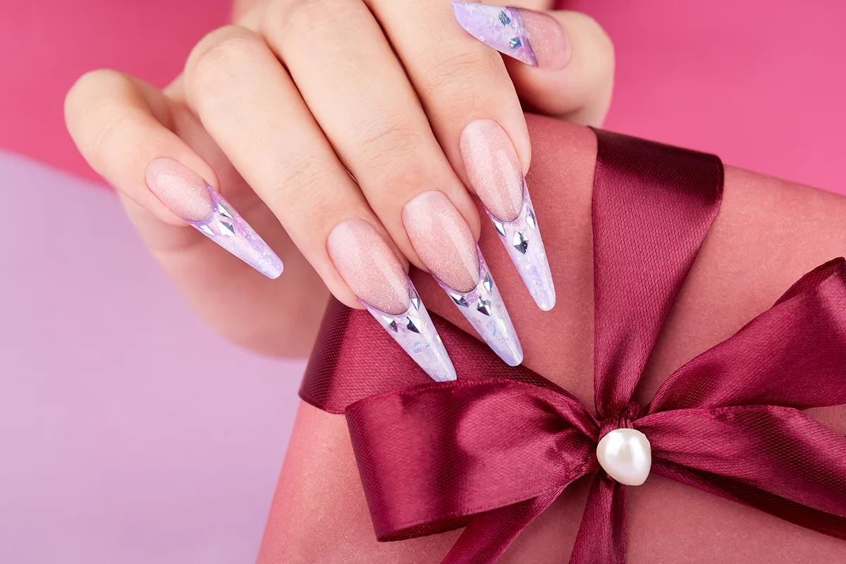Hand with long artificial french manicured nails decorated with gemstones holding a gift box.