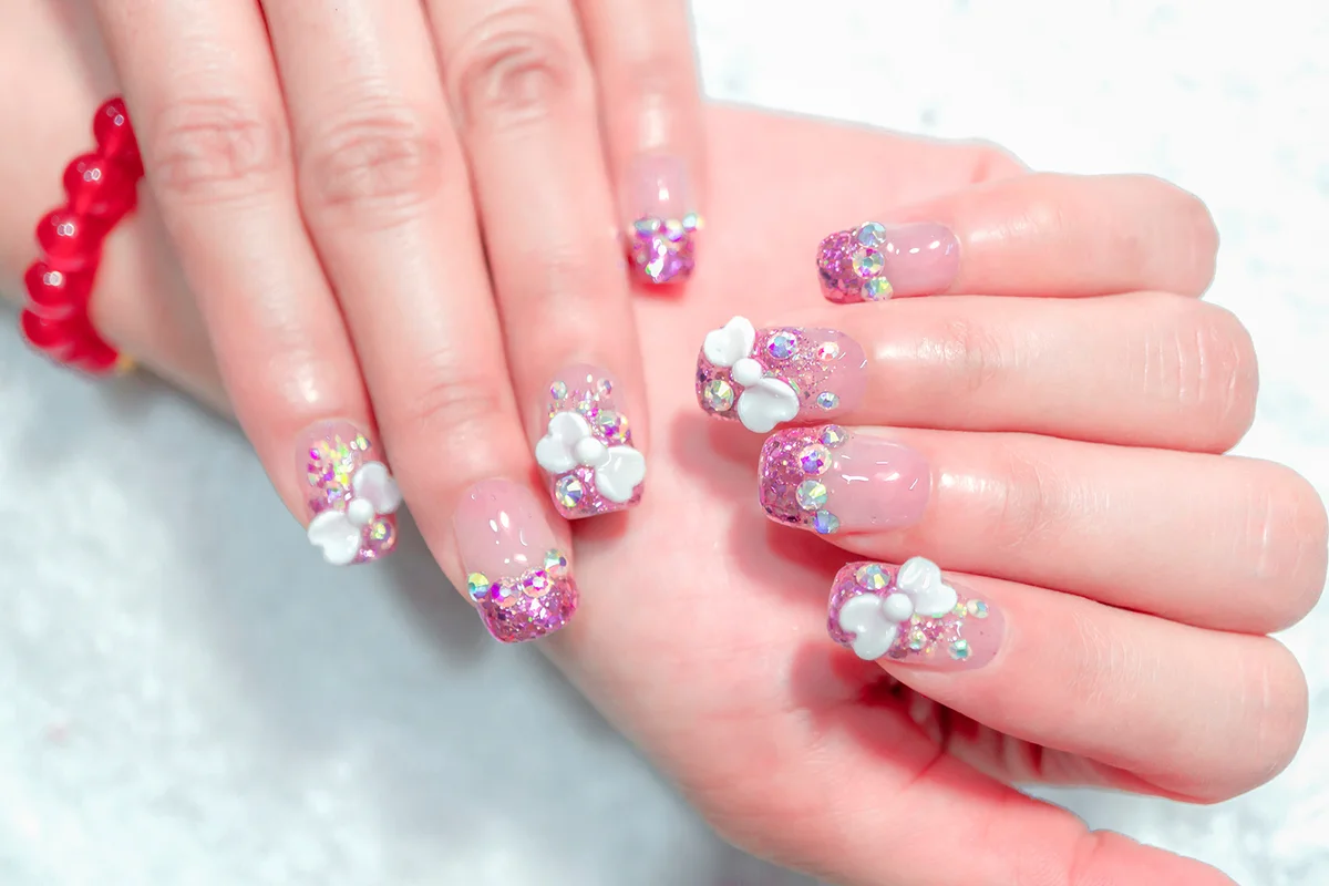 Close up Sparkling pink glitter gel nail art on fashionista woman fingernail decorated with shiny rhinestone and cute white 3D ribbon