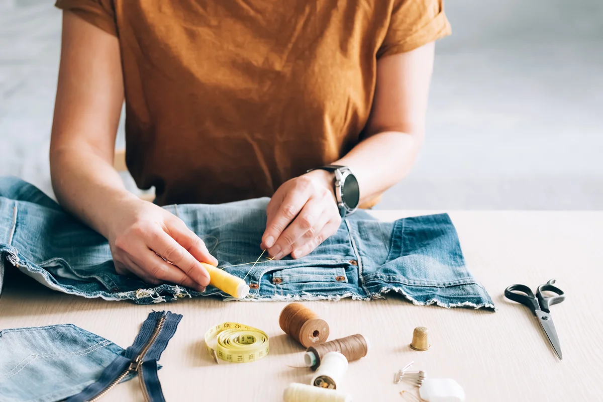 Woman repairs sews reuses fabric from old denim clothes economical reuse