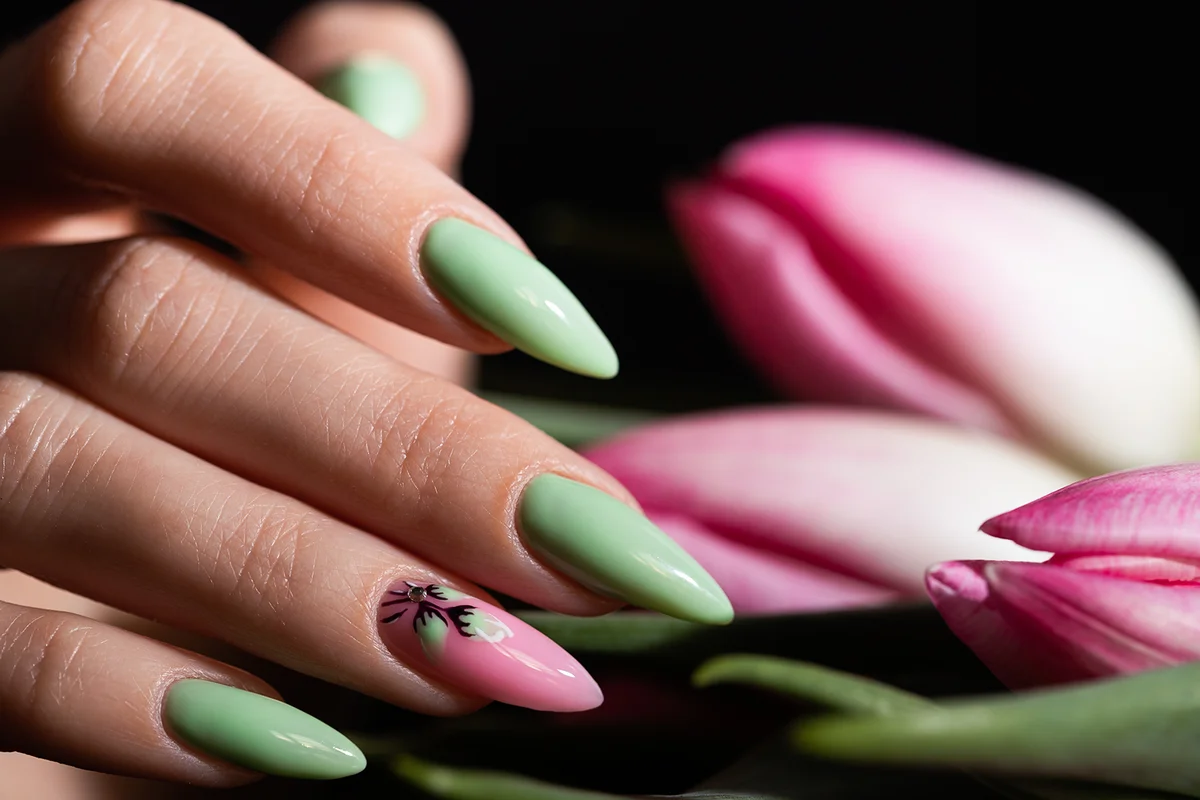 Girl's hand with a beautiful summer manicure in light green and pink color decorated with drawing of flowers
