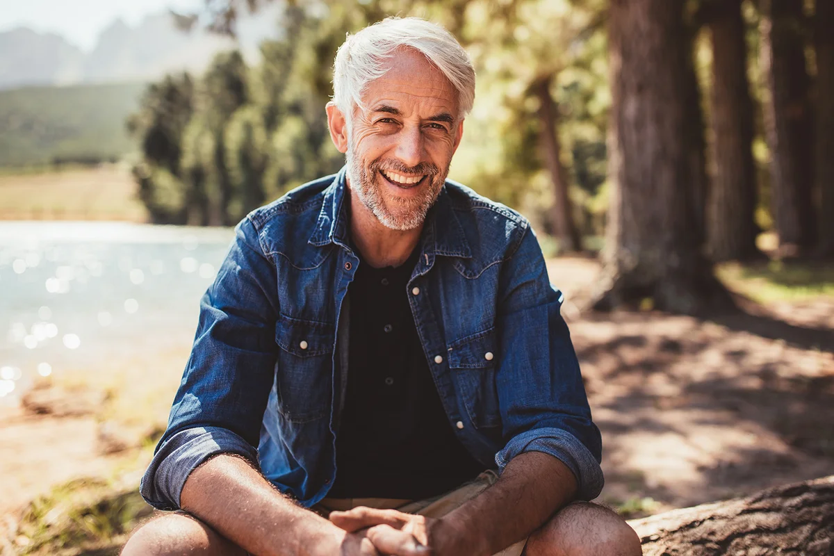man sitting near a lake looking at camera and smiling