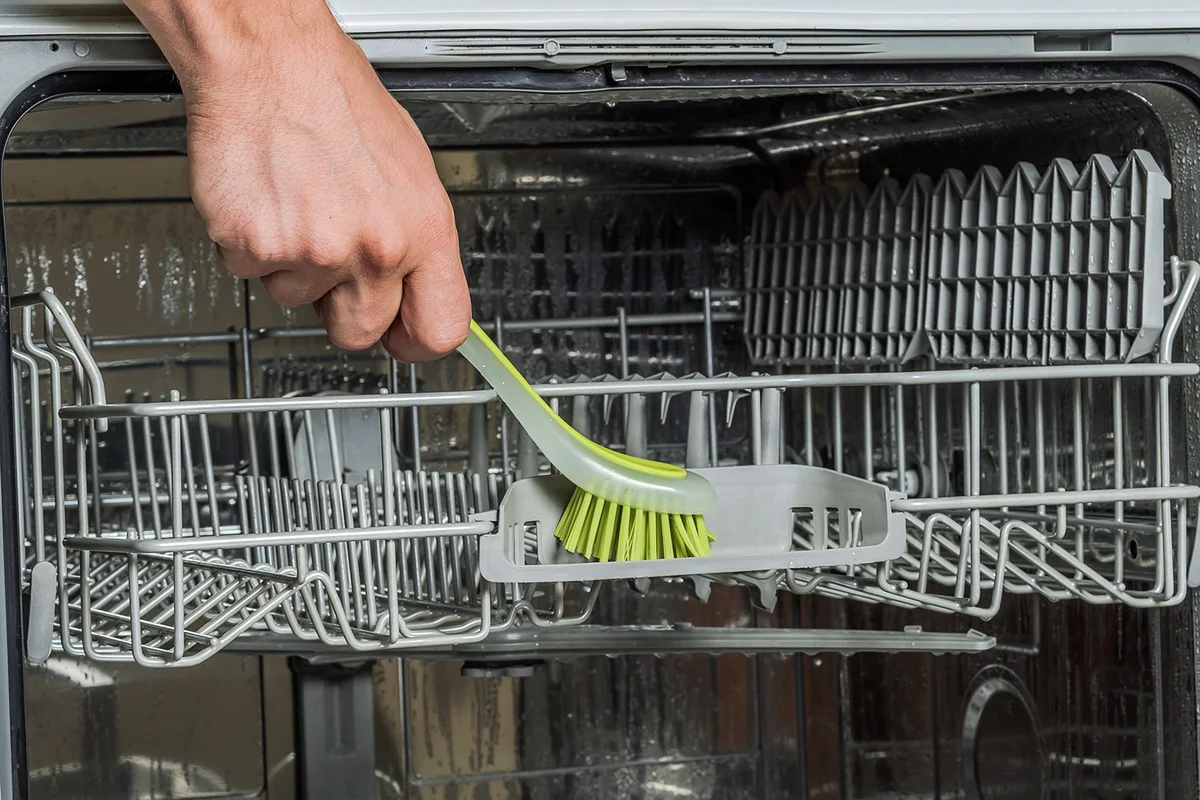 A man's hand brushes a dishwasher machine