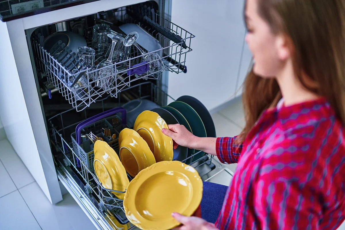 woman uses modern dishwasher for wash dishes and glasses at home kitchen