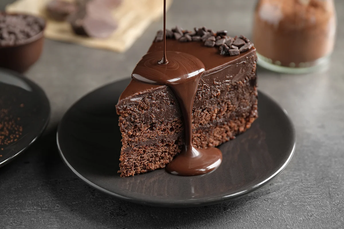 Pouring chocolate sauce onto delicious fresh cake on grey table