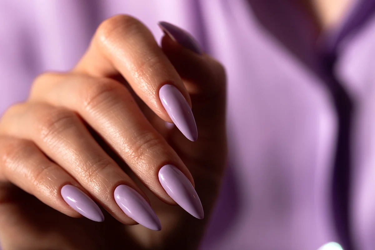 Hand with a beautiful purple long nails manicure against the background of a blurred silhouette of a girl in a lilac blouse