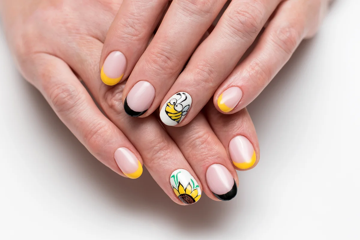 yellow French manicure with painted sunflowers and a bee on short oval nails on a white background