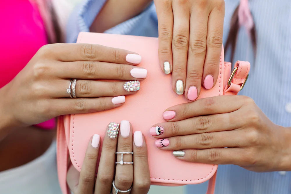 Some girl's hands beautifully manicured over a pastel neon pink bag's surface