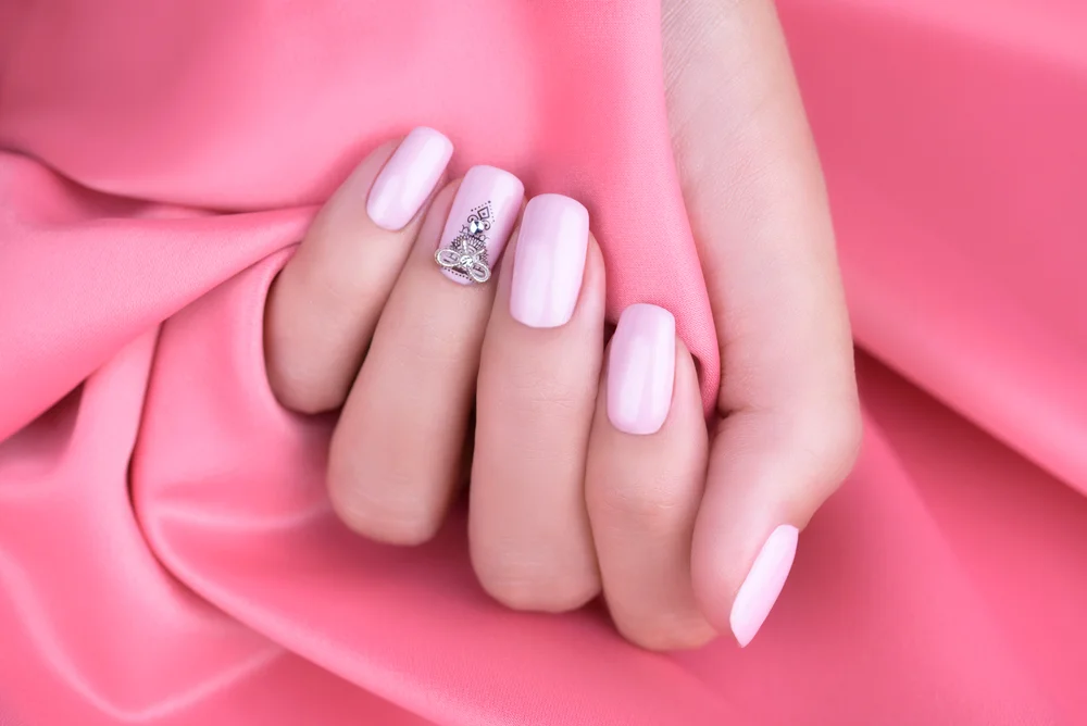Pastel pink manicure with fine details in black and a bow on a hot pink silk fabric background