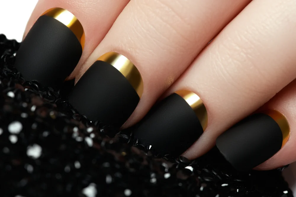 Extreme close-up of matte black nails with gold french manicure