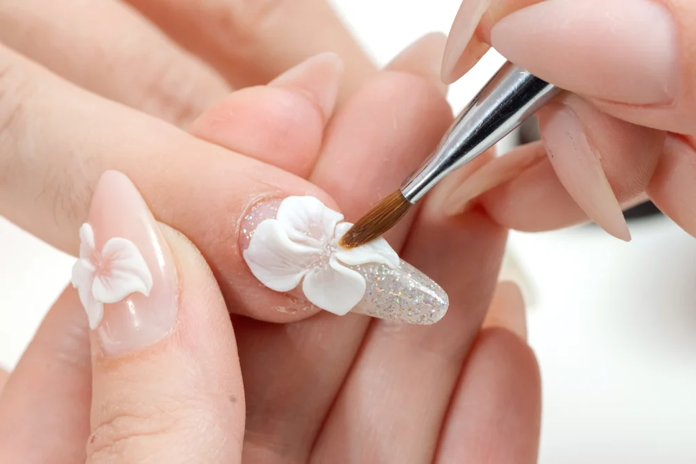 Beautiful detail of a brush painting the flower of a glitter embellished manicure.