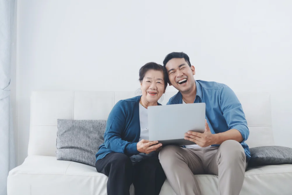 Asian man at home with his mother writing on a computer