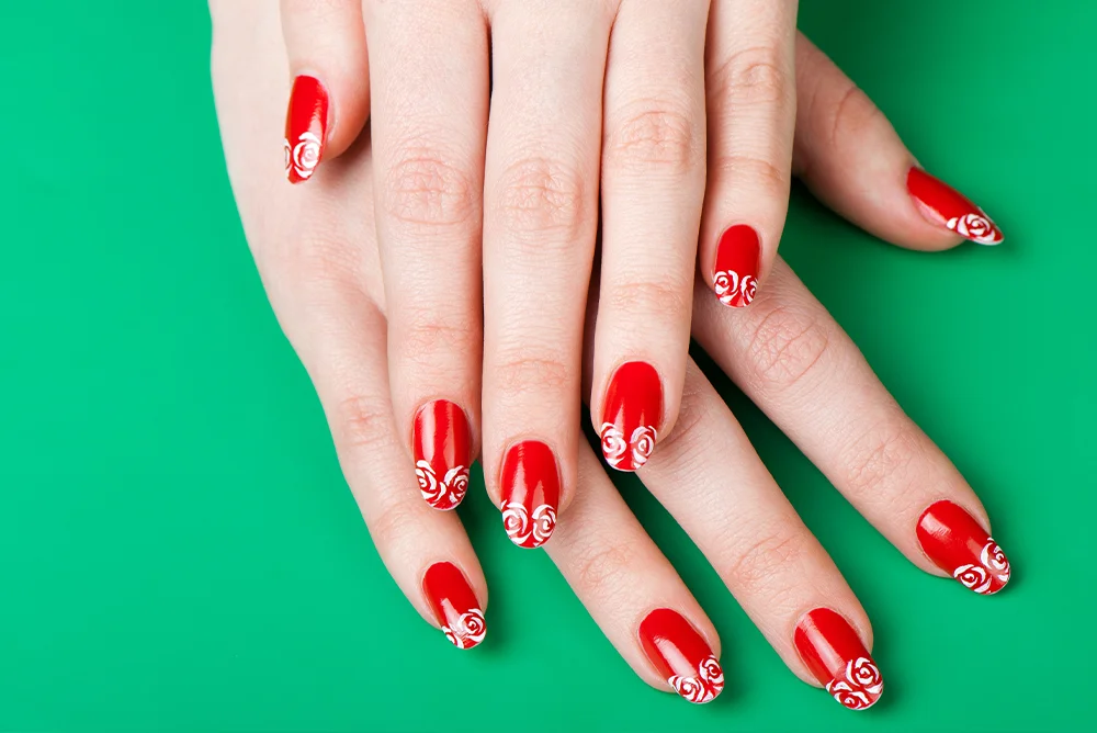 Red nails with hand-drawn white roses on a green background